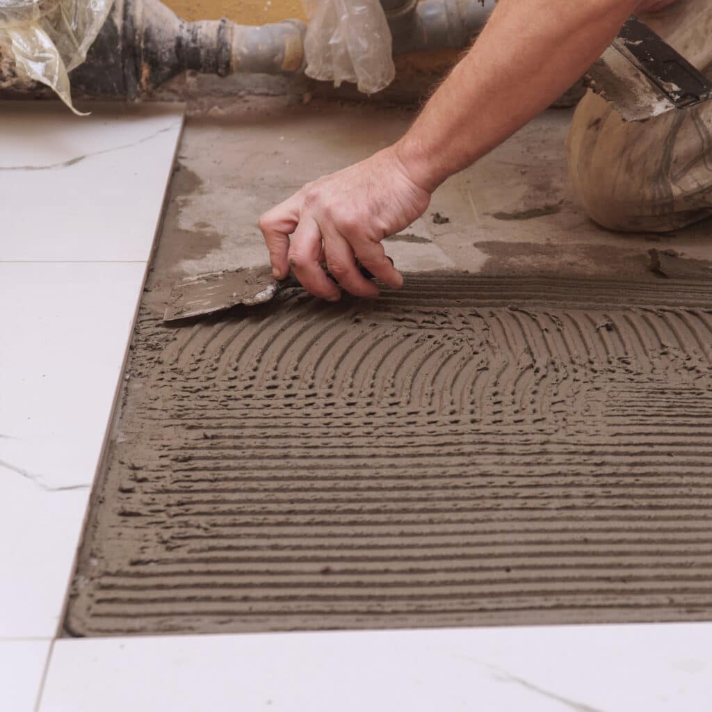 Construction worker applies cement for laying floor ceramic tiles with spatula