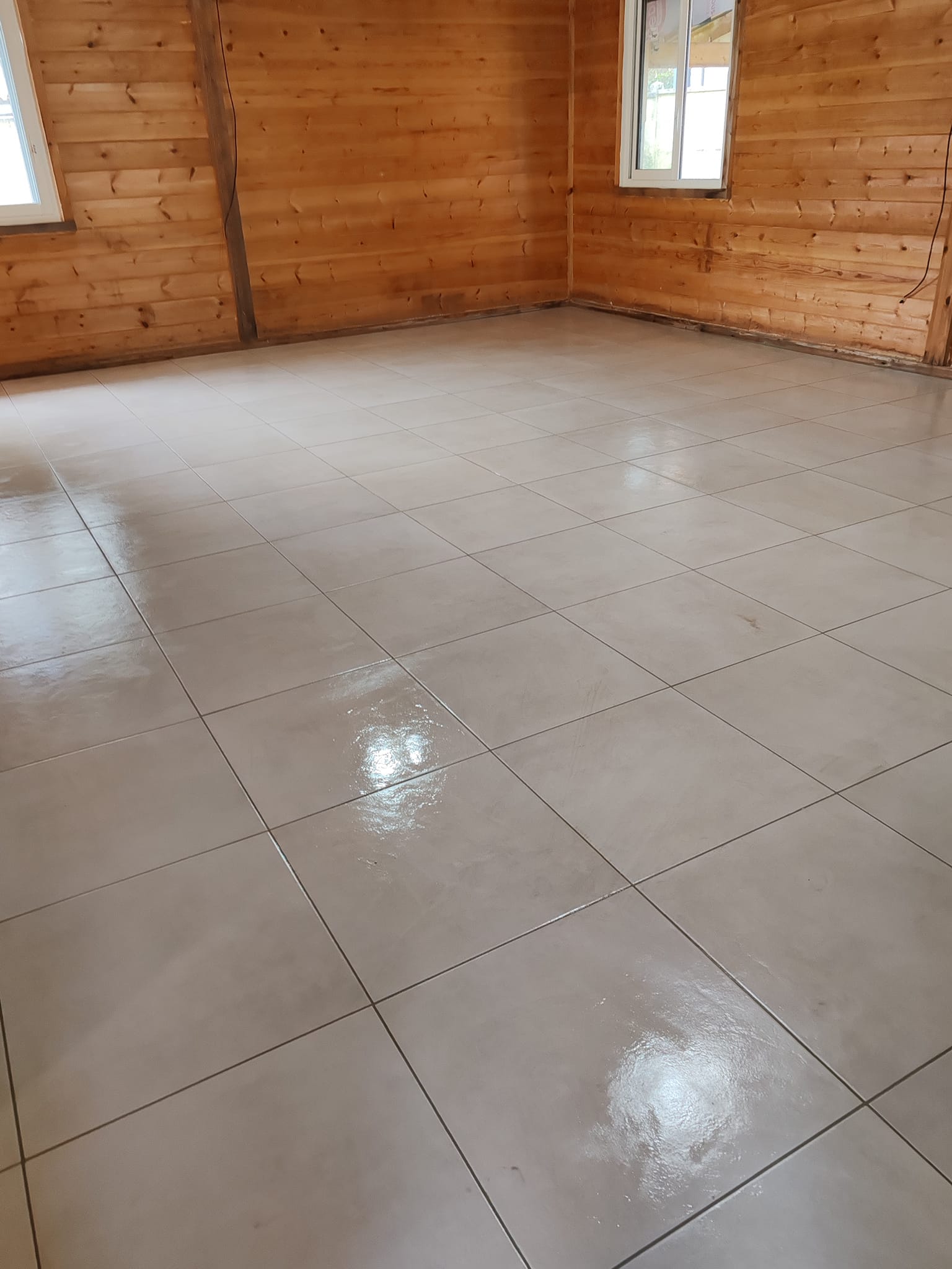 Carrelage gris clair brillant posé dans un chalet aux murs en bois rustiques avec lumière naturelle.