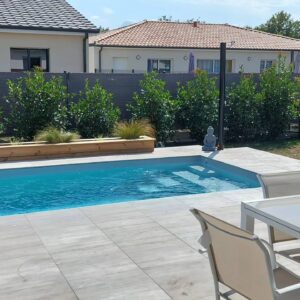 Piscine avec terrasse carrelée grise, jardinière en bois et statue de Bouddha zen dans un jardin moderne.