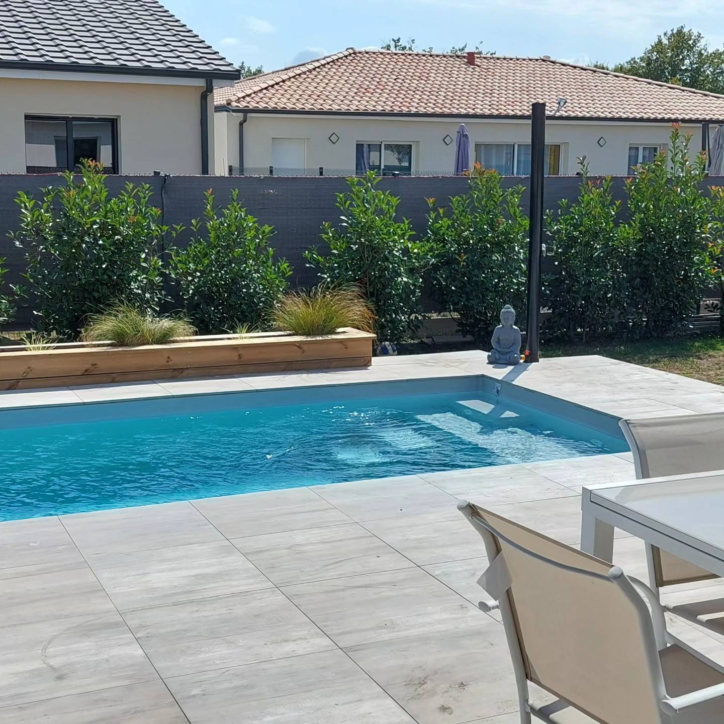 Piscine avec terrasse carrelée grise, jardinière en bois et statue de Bouddha zen dans un jardin moderne.
