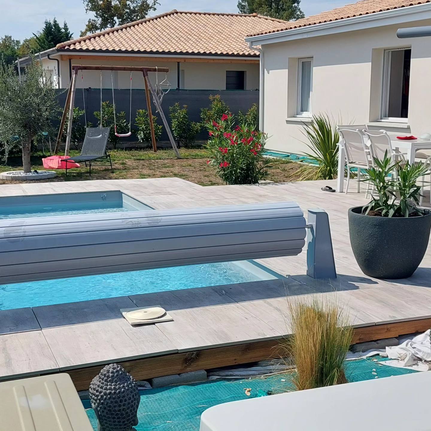 Aménagement piscine avec volet roulant, terrasse bois et statue Bouddha dans un jardin contemporain.