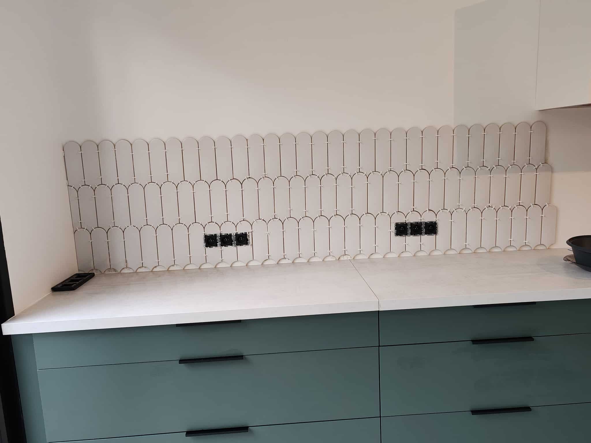 Pose de carrelage arche blanc pour une crédence de cuisine avec meubles bas vert canard et plan de travail blanc.