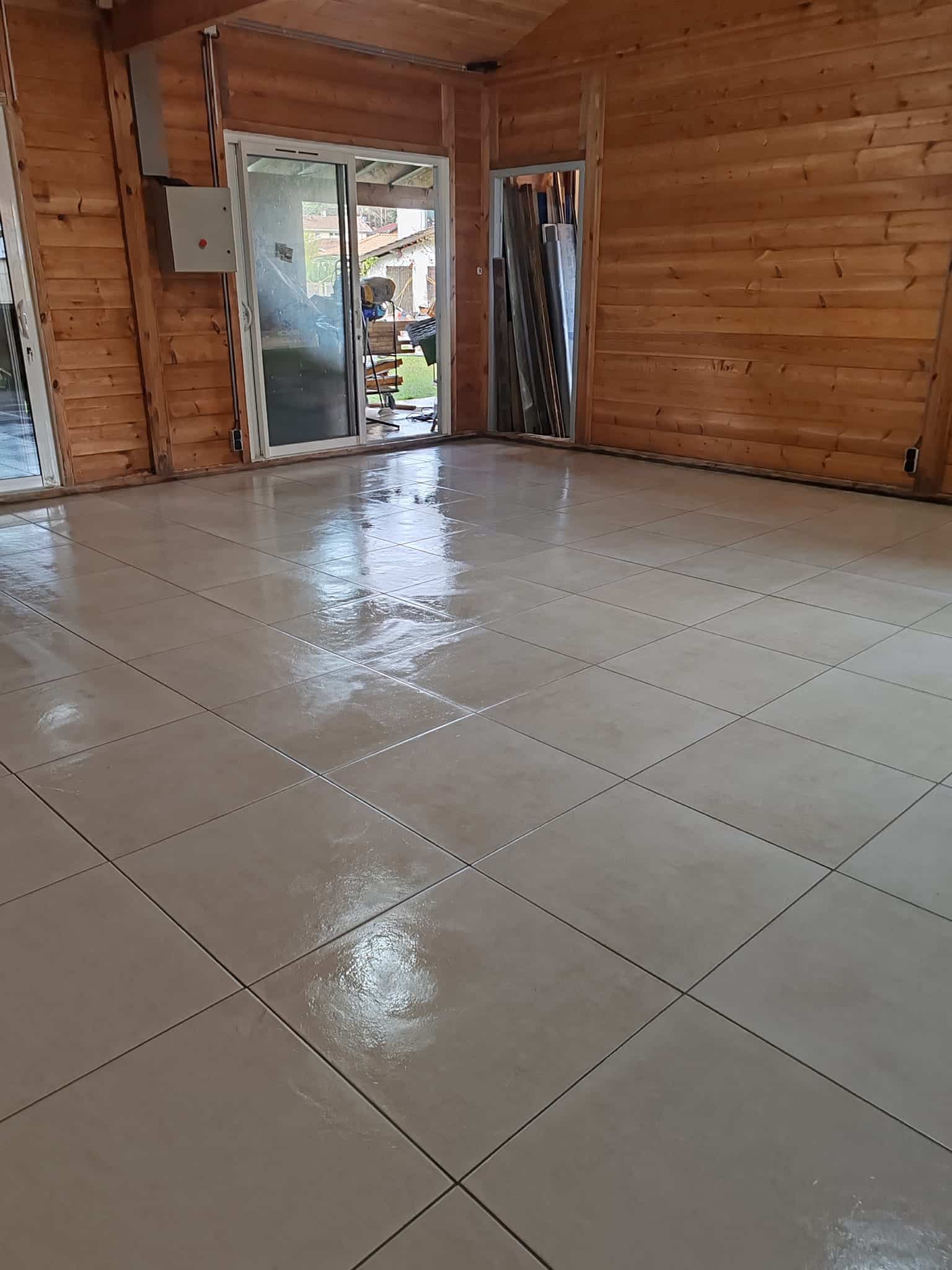 Intérieur de chalet avec carrelage beige brillant et murs en bois clair, reflet lumineux sur le sol fraîchement poli.