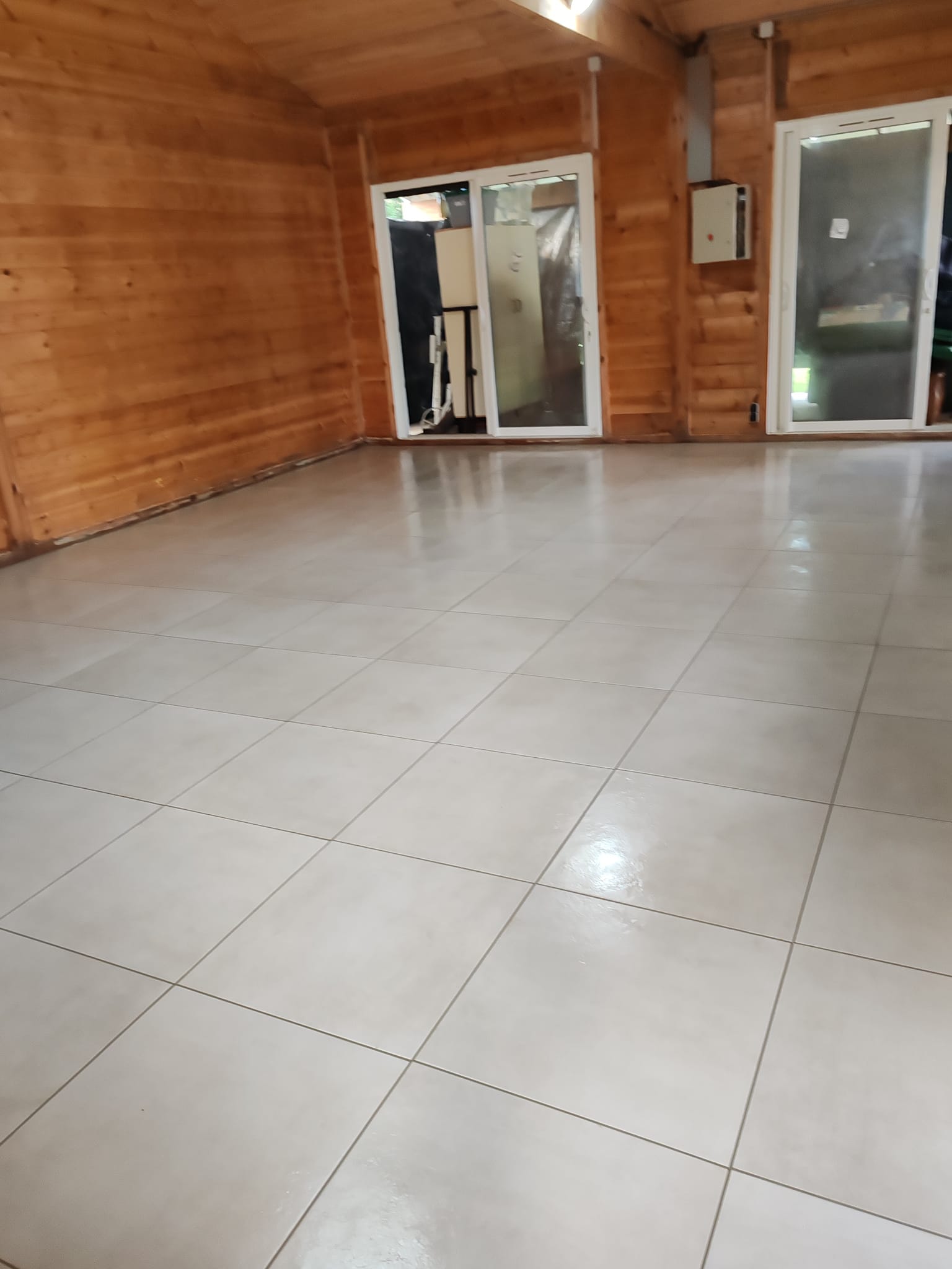 Intérieur d'un chalet en bois avec un carrelage gris brillant au sol et des grandes baies vitrées coulissantes.