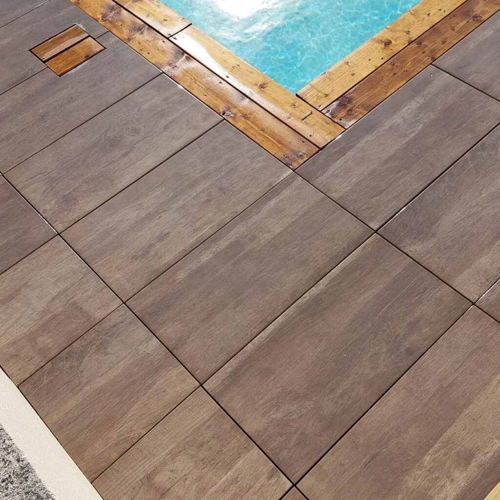 Carrelage de Terrasse Imitation Bois pour une Piscine Moderne Dalles de terrasse imitation bois gris près d'une piscine avec bordure en bois naturel et eau bleue limpide.