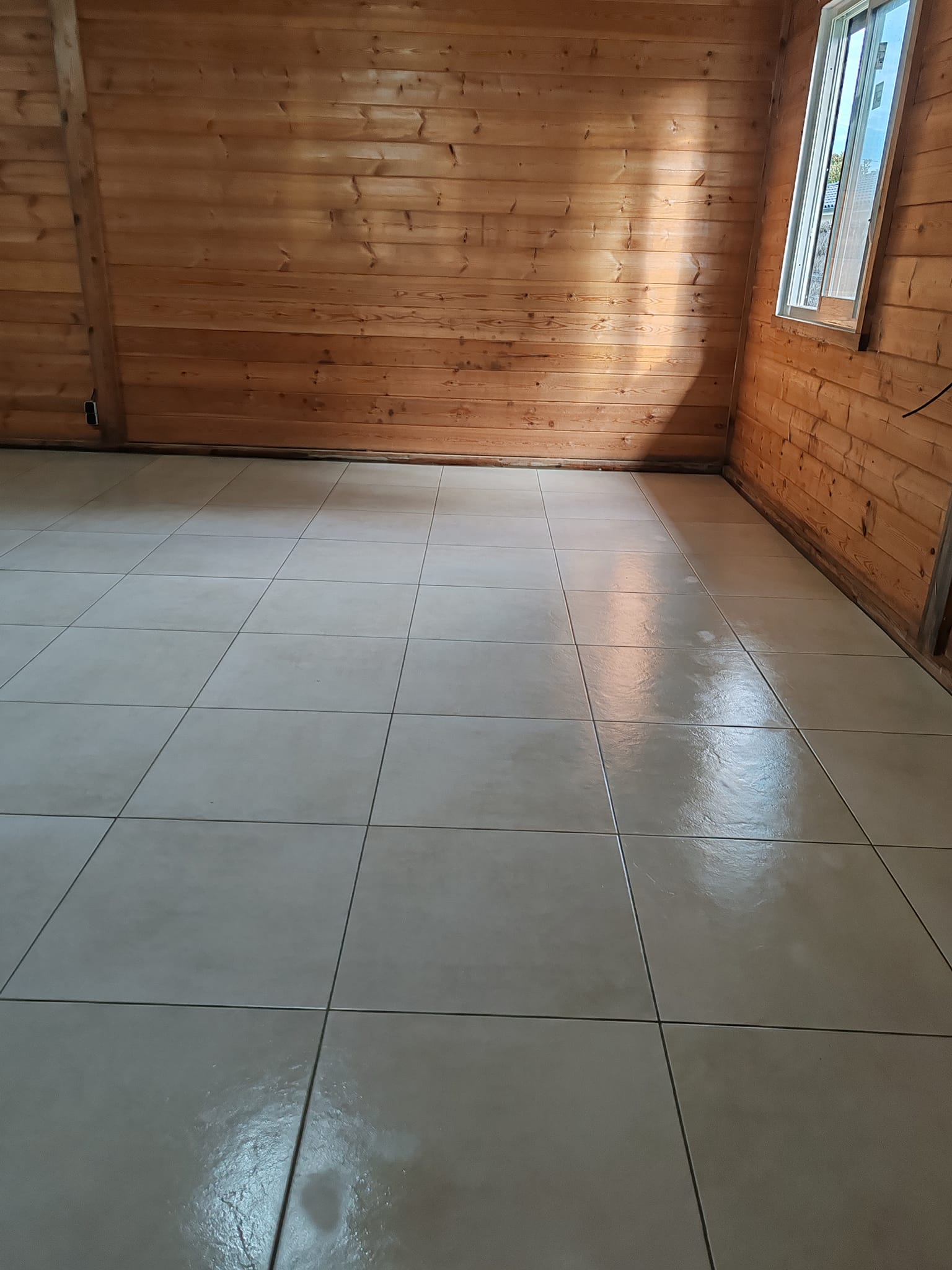 Intérieur d'un chalet avec murs en bois et sol en grand carrelage beige brillant reflétant la lumière.