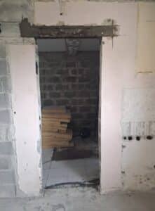 Ouverture de porte dans un mur en parpaings avec linteau en béton apparent sur un chantier de rénovation intérieure.