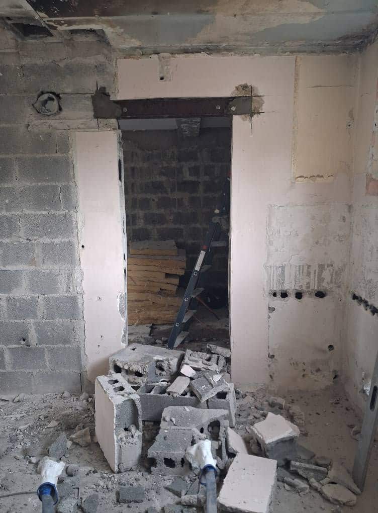 Ouverture de porte dans un mur en parpaings avec linteau acier et gravats au sol sur un chantier de rénovation.