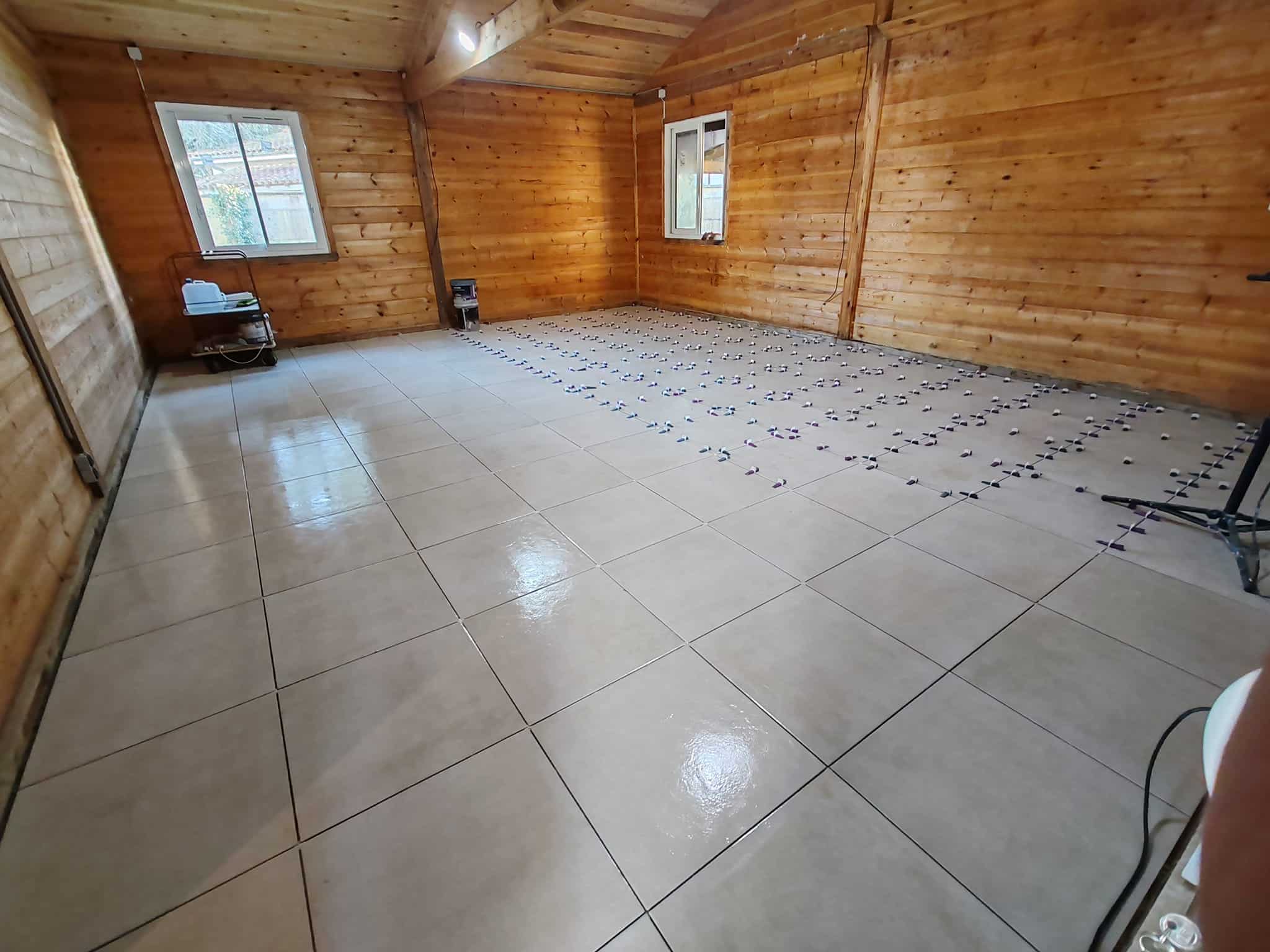Pose de carrelage beige dans une pièce en bois avec croisillons de nivellement pour un sol parfaitement plat.