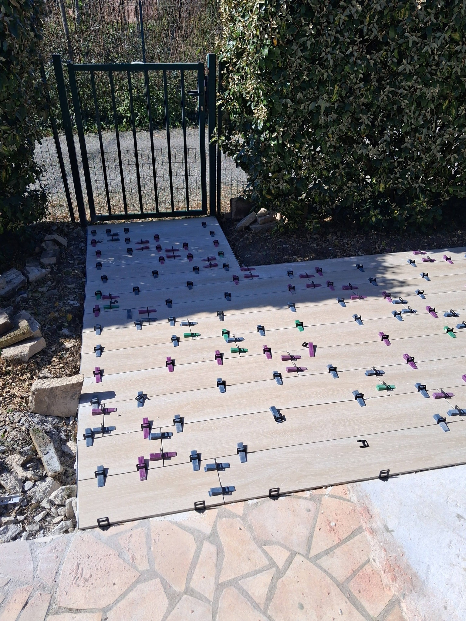 Carrelage extérieur aspect bois en cours de pose avec croisillons autonivelants devant un portillon de jardin.