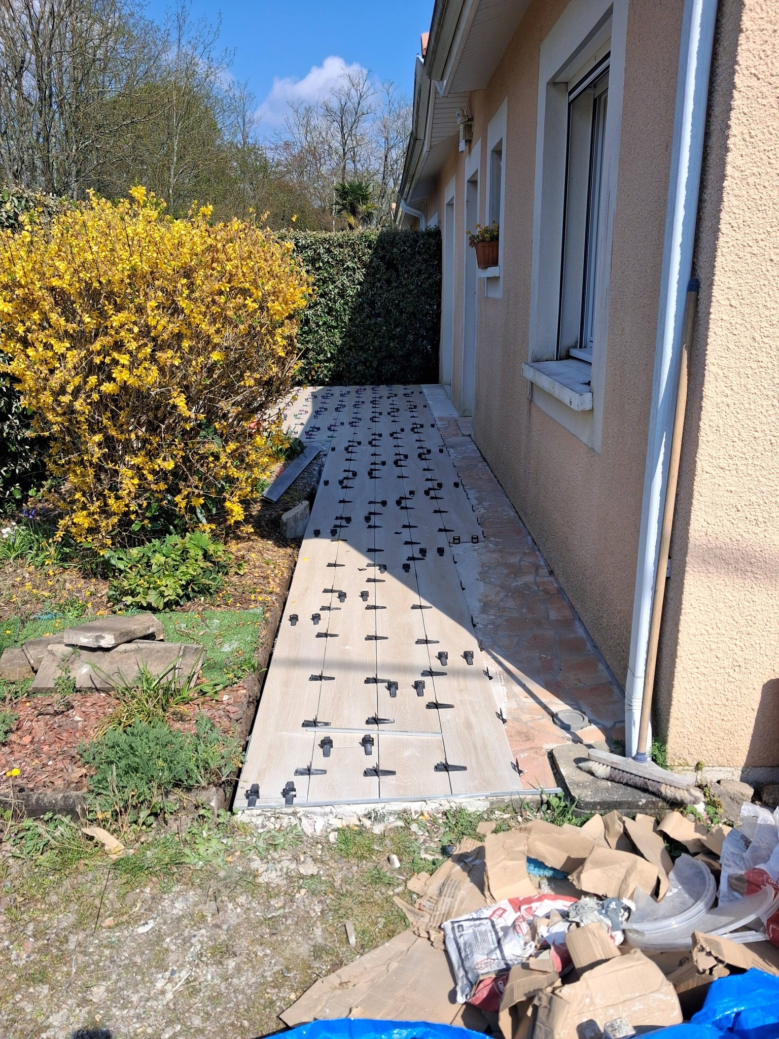 Pose de carrelage effet bois sur terrasse extérieure avec croisillons autonivelants noirs le long d'un mur.