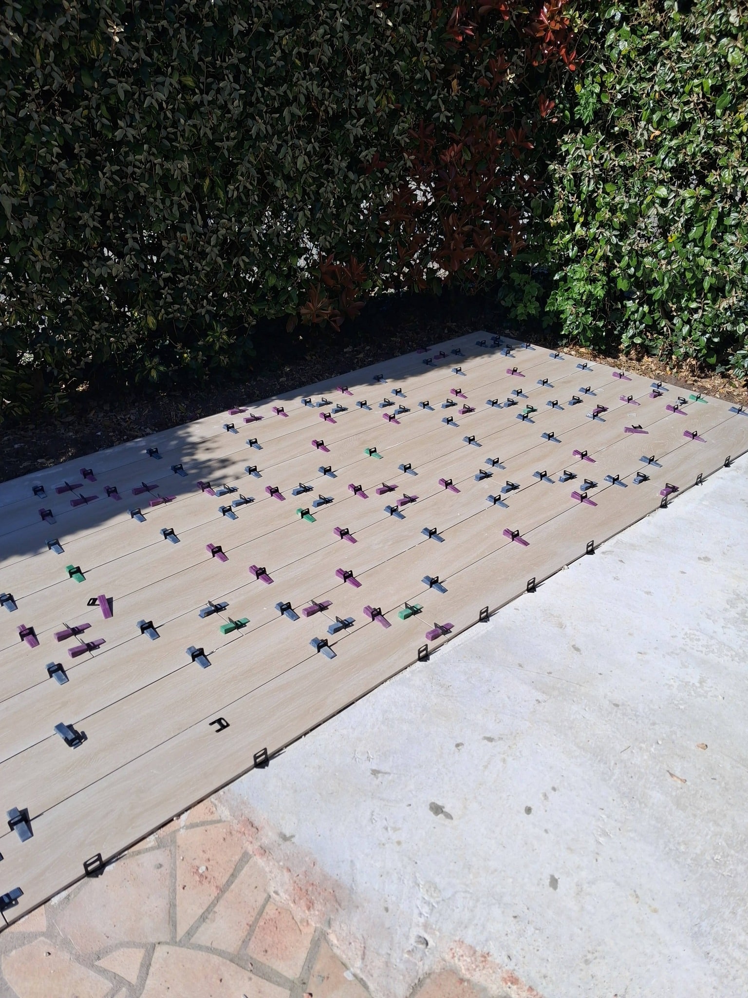 Pose de carrelage extérieur aspect bois avec croisillons autonivelants sur une terrasse en cours de travaux.