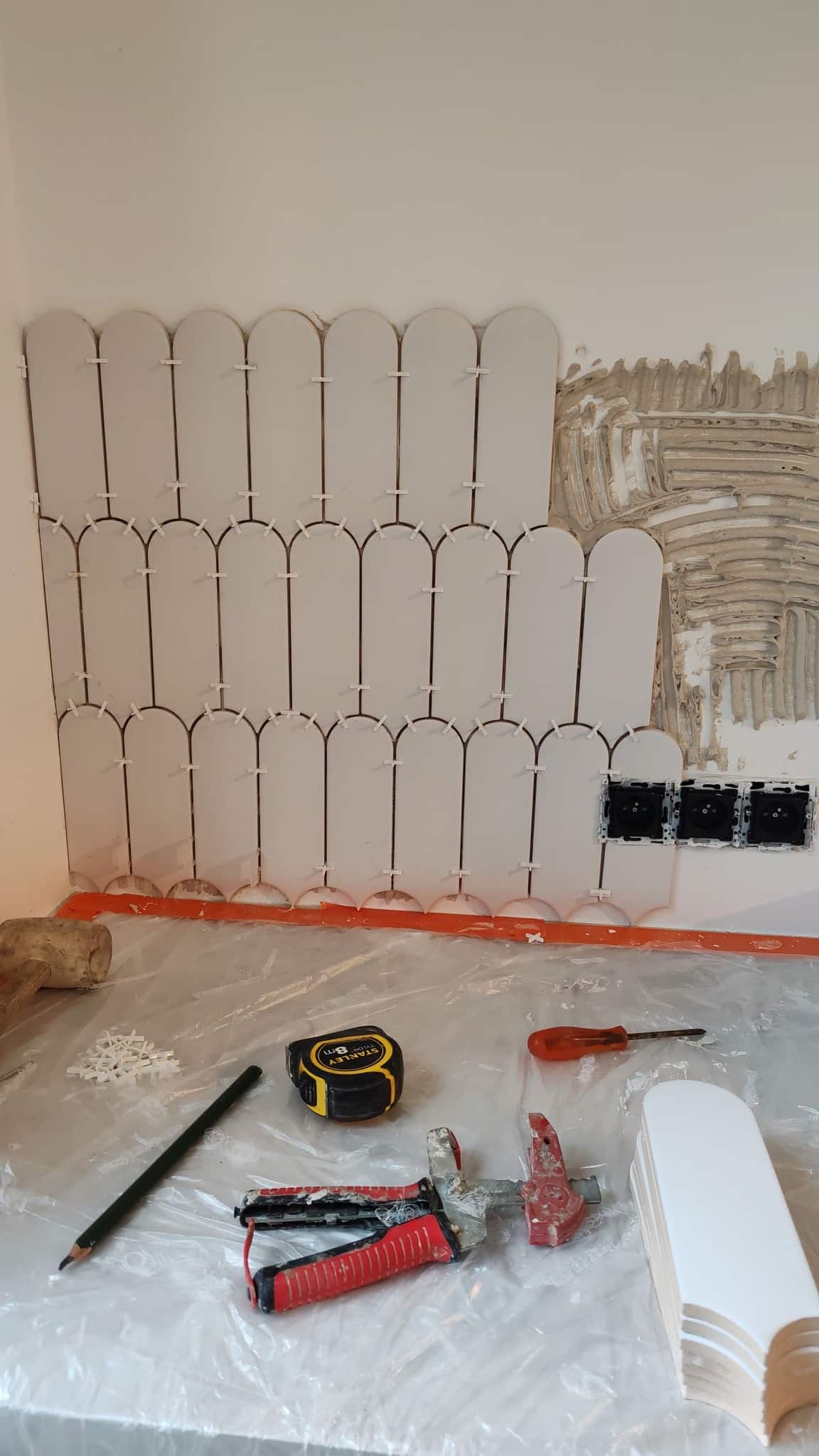 Pose de carrelage mural blanc en forme d'arches avec croisillons et outils de bricolage sur le plan de travail.