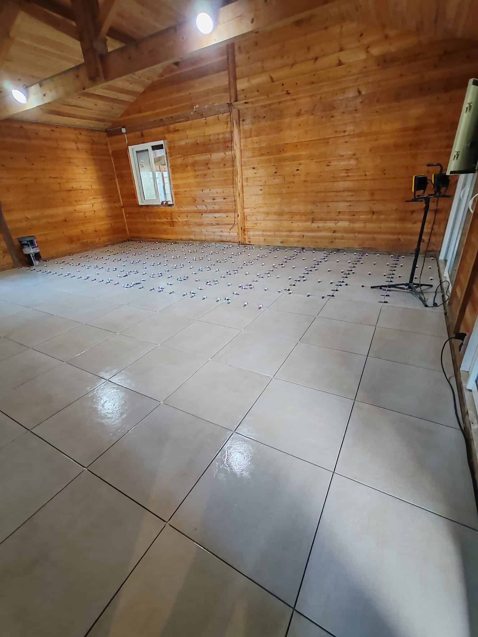 Pose de carrelage au sol dans une pièce en bois avec système de nivellement et carreaux grand format.