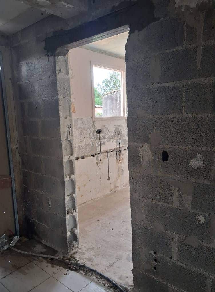 Ouverture de porte dans un mur en parpaings lors de travaux de rénovation avec linteau apparent.