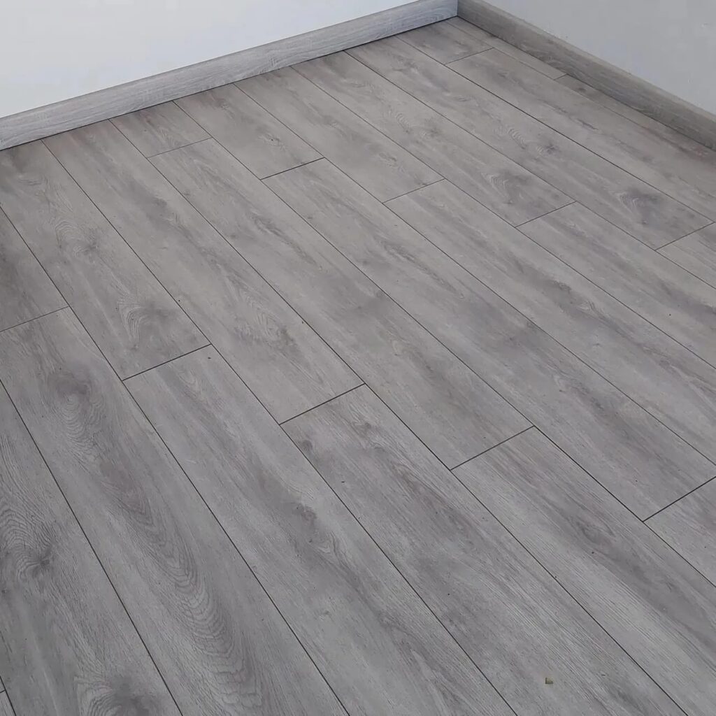 Sol Stratifié Gris Effet Bois : Pose Moderne et Épurée Revêtement de sol en stratifié gris clair avec texture imitation bois et plinthes assorties dans une pièce moderne.
