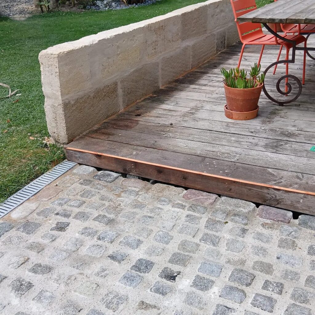 Aménagement de terrasse en bois avec pavés et muret Terrasse extérieure en bois bordée d'un muret en pierre, avec patio en pavés, chaise rouge et plante en pot.
