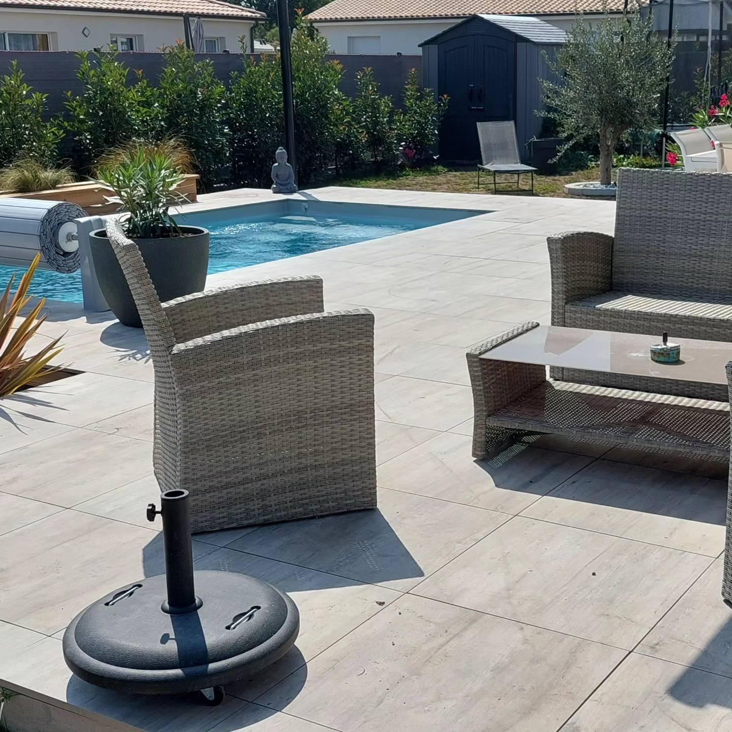 Salon de jardin en résine tressée grise près d'une piscine sur une terrasse moderne avec base de parasol.