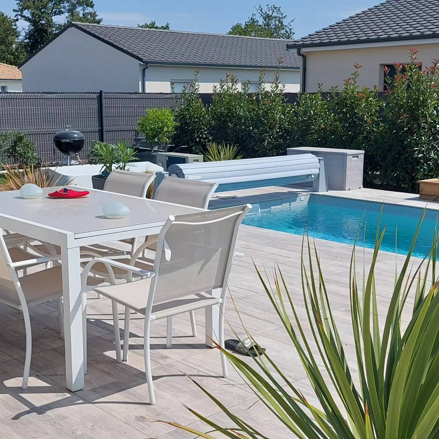 Table de jardin blanche et chaises devant une piscine avec couverture automatique sur une terrasse moderne.